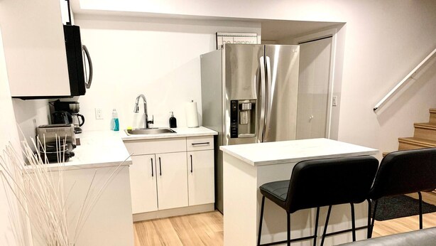 A compact kitchen with a refrigerator, sink, and a small dining area with two chairs. - Royal Oak- 2-bedroom Suite (Winnipeg)