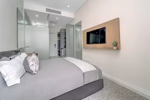 Ein modernes Schlafzimmer mit Bett, Wandfernseher und begehbarem Kleiderschrank.