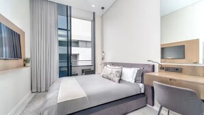 Ein modernes Hotelzimmer mit Bett, Schreibtisch, Stuhl, Fernseher und einem großen Fenster.