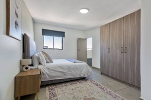 Ein Schlafzimmer mit Bett, Nachttisch, Lampe, Kleiderschrank und Fenster.