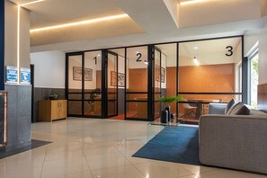 Eine moderne Hotelhalle mit Glastüren, durchnummeriert von 1 bis 3, einem Empfangstisch, einer Couch und einem blauen Teppich.