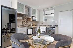 A modern kitchen with a glass-top dining table, grey upholstered chairs, and a stainless steel refrigerator. - Spacious Two-bedroom Apartment in Rosebank (Johannesburg)