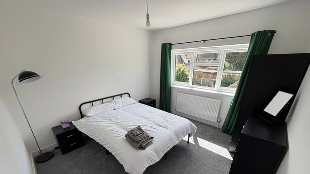 Een slaapkamer met een bed, een bureau, een lamp, een radiator en een raam met gordijnen.