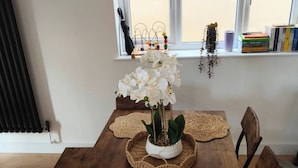 Een eettafel met geweven placematen, een potorkidee en een decoratief object op de vensterbank.
