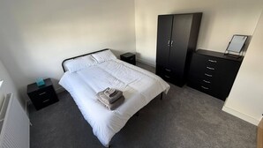 Een slaapkamer met een bed, een kledingkast, een nachtkastje en een radiator.