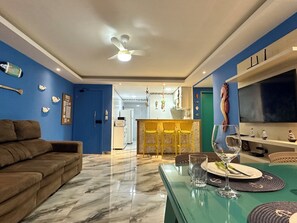 Ein modernes Wohnzimmer mit einer Couch, einem Esstisch mit Stühlen, einem Fernseher und einem Deckenventilator.