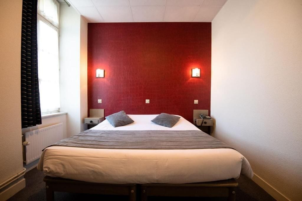 Quarto de hotel com uma cama, duas mesas de cabeceira, uma janela com cortinas e duas luzes fixadas na parede.