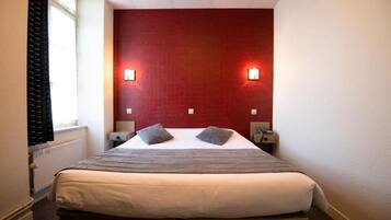 Quarto de hotel com uma cama, duas mesas de cabeceira, uma janela com cortinas e duas luzes fixadas na parede.