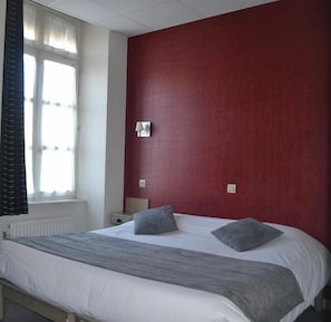 A bedroom with a bed, a window with curtains, a nightstand, and a red wall. - L Espérance (Vitré)