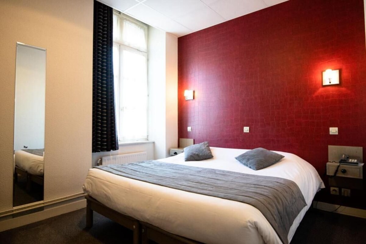 Una habitación de hotel con cama, mesita de noche, espejo y ventana con cortinas.