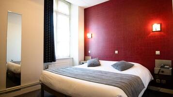 A hotel room with a bed, a nightstand, a mirror, and a window with curtains.