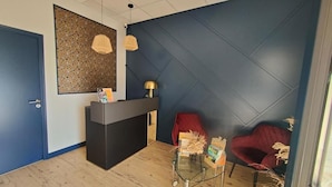 A reception area with a dark blue wall, a reception desk, two red chairs, and a glass table with a vase. - L Espérance  (Vitré)