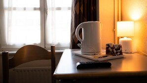 A hotel room with a table, a coffee maker, two mugs, a remote control, and a lamp. - L Espérance  (Vitré)