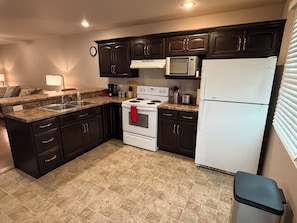 A kitchen with dark cabinets, a white stove, a microwave, and a refrigerator.