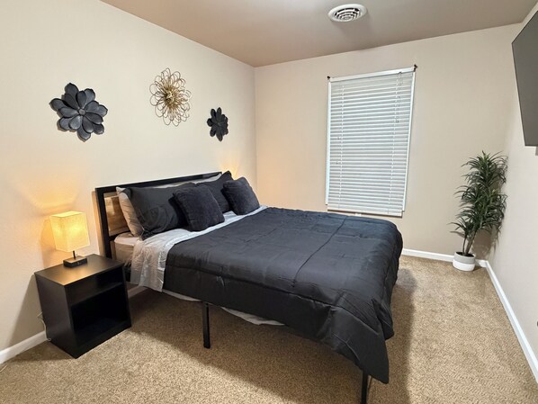 A bedroom with a bed, nightstand, lamp, wall art, window, and a potted plant.