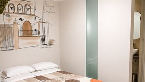A bedroom with a bed, a wall-mounted artwork, a bedside table, and a bathroom door.