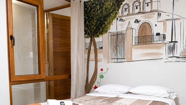 A bedroom with a bed, a window, a plant, and a wall mural.
