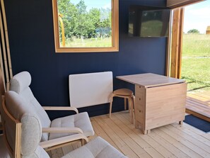 A room with a dark blue wall, a wooden desk, a white chair, a wooden stool, and a TV mounted on the wall.