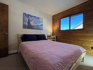 Une chambre à coucher avec un lit, une table de chevet, un tableau et une fenêtre.