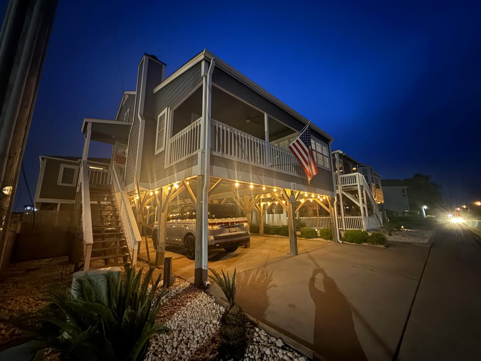 A two-story beachfront house with a covered porch and an American flag.