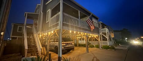 A two-story beachfront house with a covered porch and an American flag.