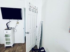 A room with a white door, a mounted television, a small white cabinet, and a chair. - OCEAN VIEWS! 3 BD / 2 BA, 3 min walk to beach! (Myrtle Beach)