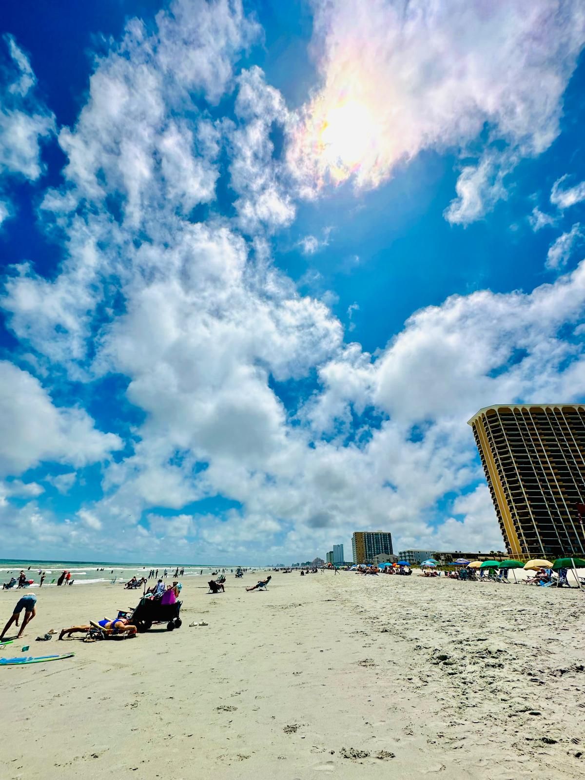 Une plage avec un grand bâtiment en arrière-plan, une plage de sable et un ciel partiellement nuageux.