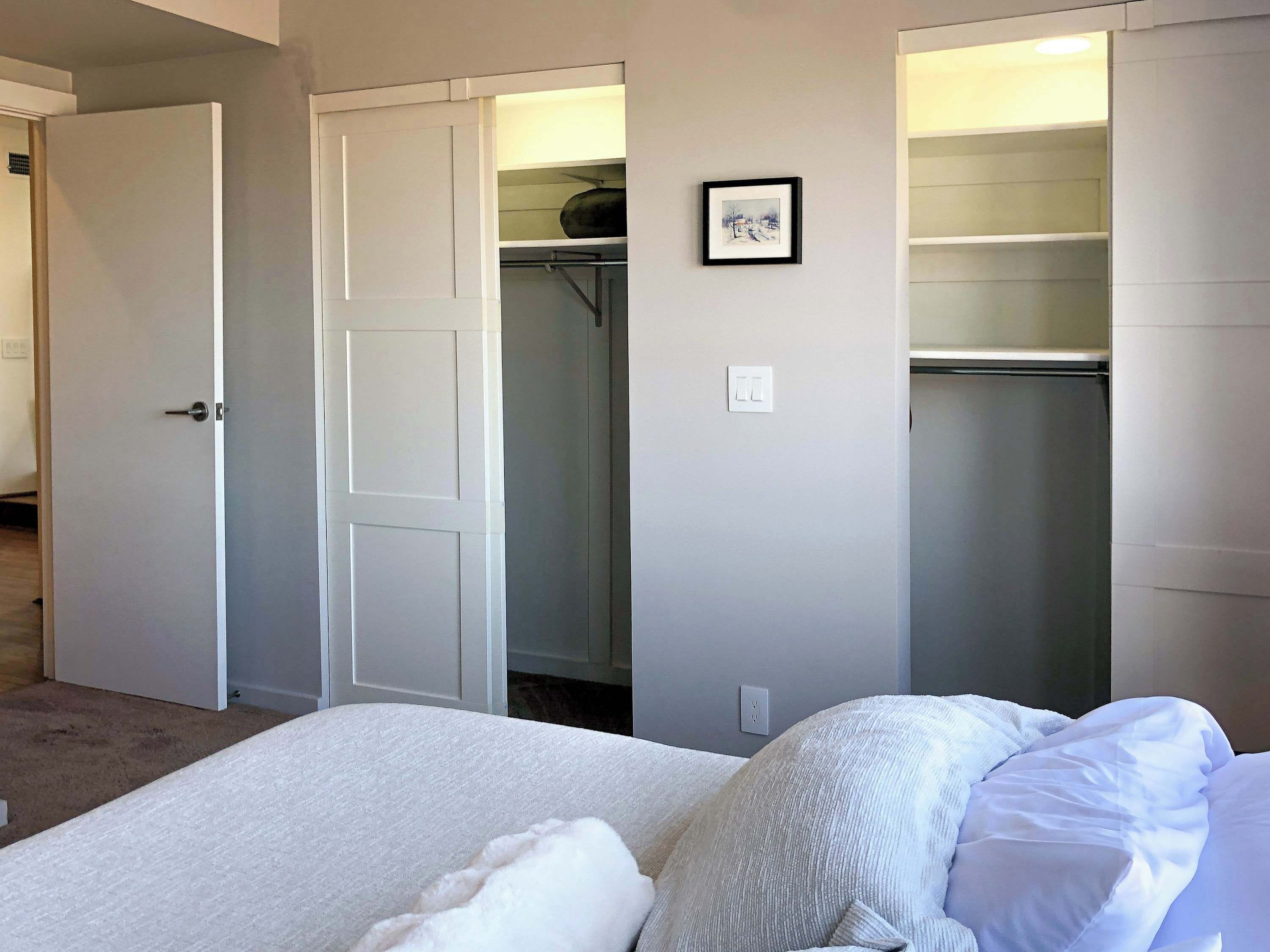 A bedroom with a bed, white bedding, a closet with a mirror, and a framed picture on the wall.