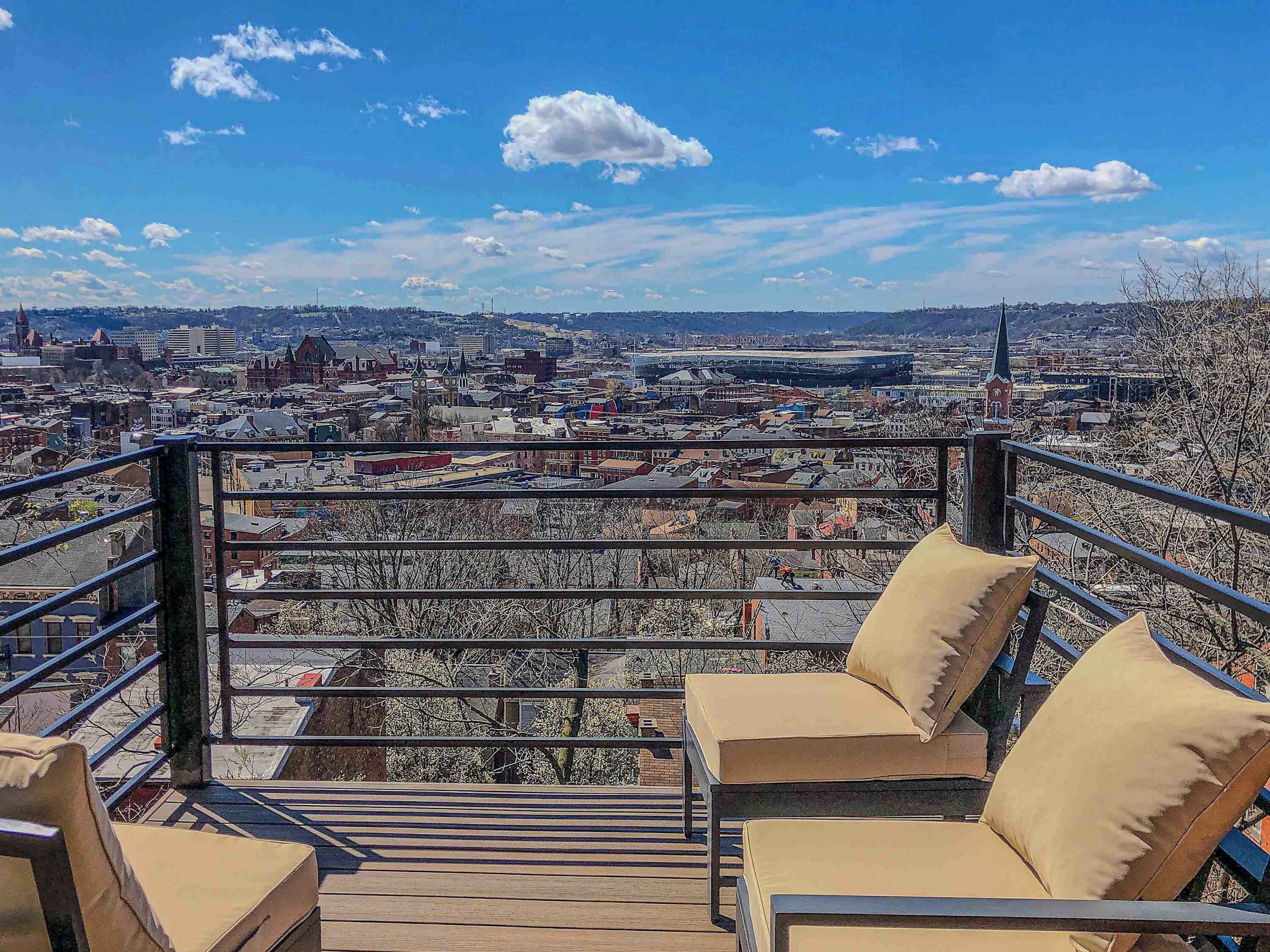 Un balcón con vista a la ciudad, barandilla y dos sillones beige acolchados.