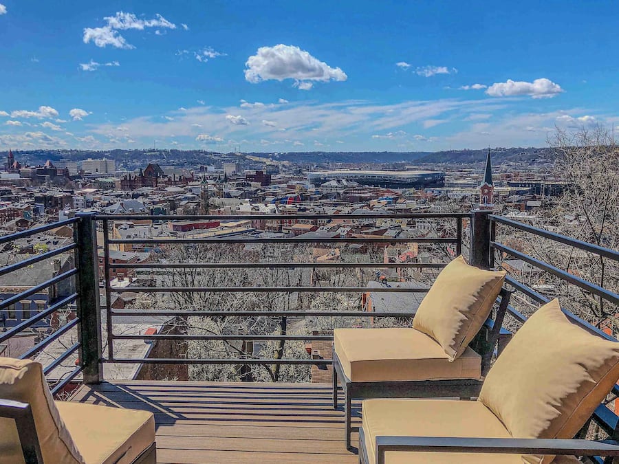 A balcony with a city view, a railing, and two beige cushioned chairs.