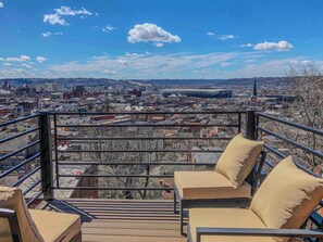 Un balcó amb vista a la ciutat, una barana i dues cadires beiges amb coixins.