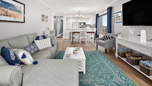 Ein modernes Wohnzimmer mit Sofa, Couchtisch und Fernseher, das in eine Küche und einen Essbereich übergeht.