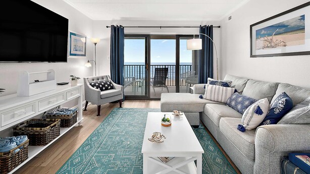 Ein Wohnzimmer mit Fernseher, Sofa, Sesseln und Blick ins Freie.