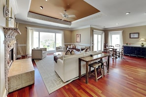A spacious living room with a fireplace, a dining area with a wooden table and chairs, and large windows allowing natural light. - Tybee Nights (Tybee Island)