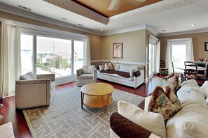 A spacious living room with large windows, a white sofa, a patterned armchair, and a round coffee table. - Tybee Nights (Tybee Island)