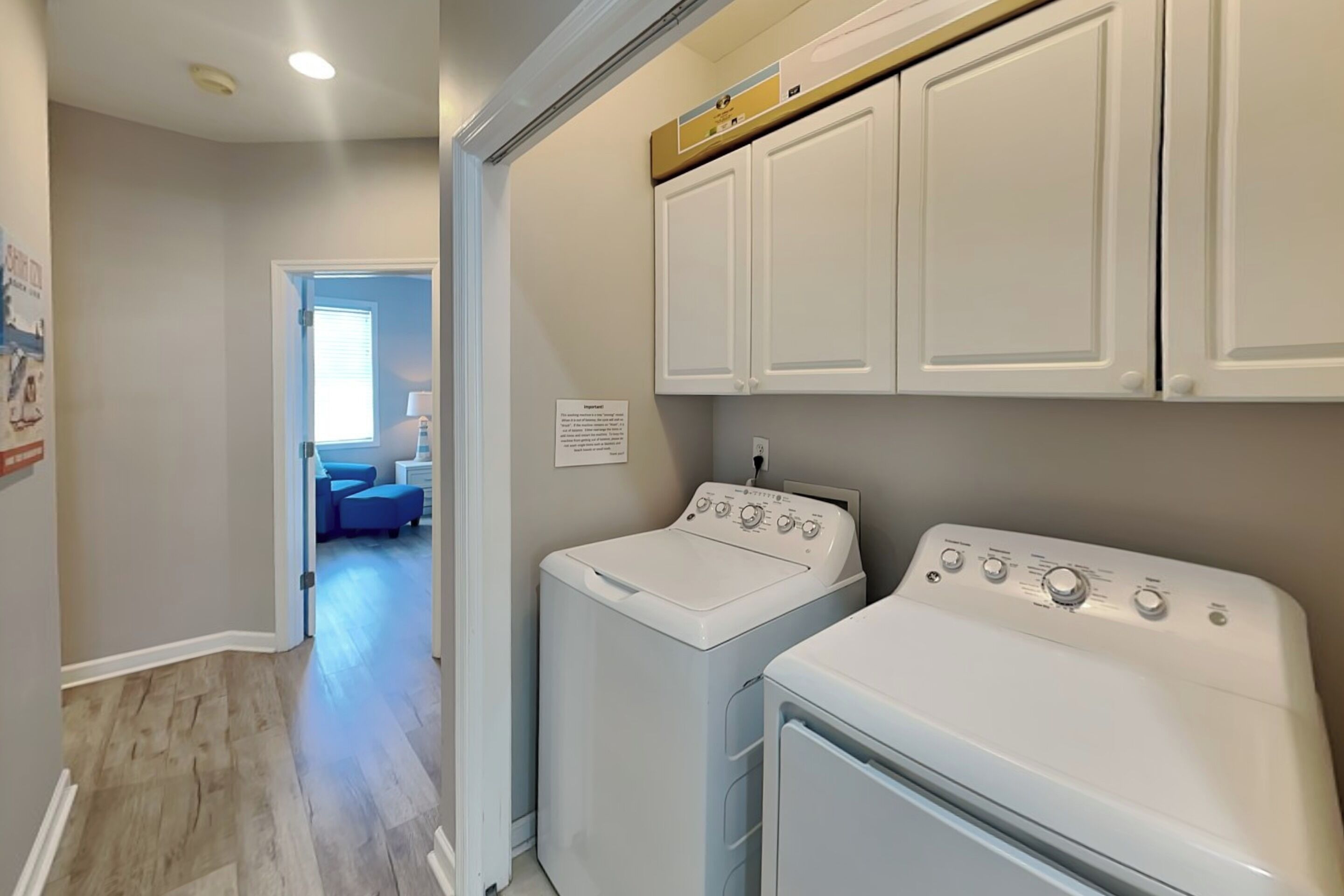 A laundry room with two white washers and dryers, a wooden floor, and a hallway leading to a living area.