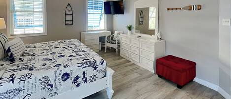 A bedroom with a bed, dresser, vanity, and a red bench.
