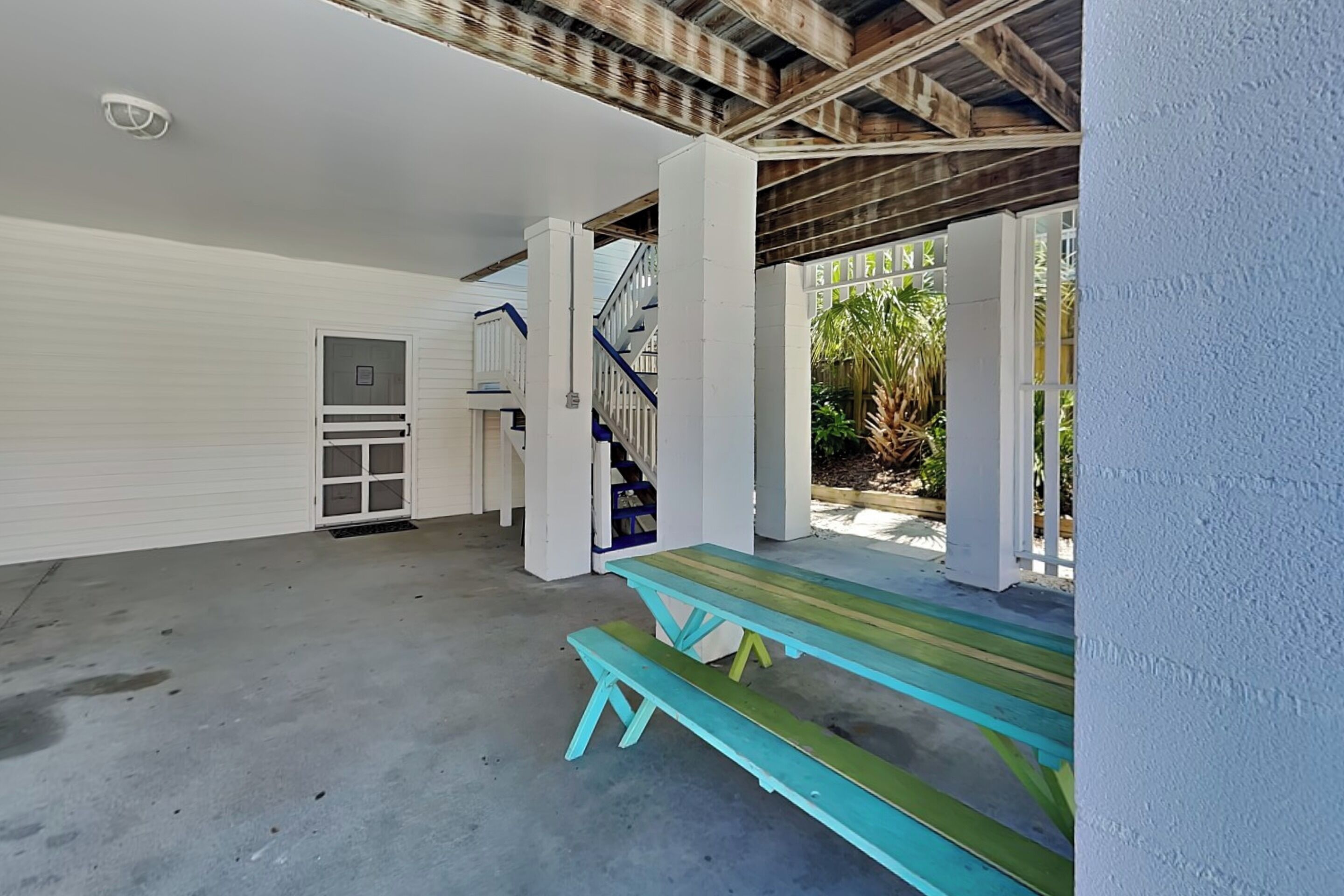 A covered outdoor area with a picnic table and benches, a staircase, and a door leading to an enclosed space.