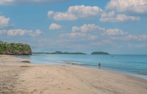 Una playa con cielos despejados, agua tranquila y islas a lo lejos.