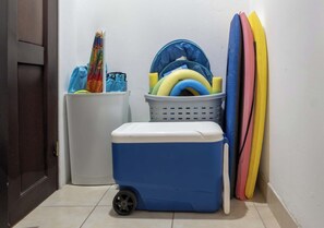 Een hoekje met een blauwe koelbox, een witte prullenbak en een mand met kleurrijke spullen.