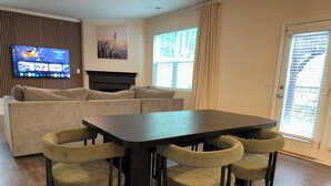 A modern living room with a sofa, a TV, a fireplace, and a dining table with chairs. - Family Friendly and Group Stay 4BR Home, Sleeps 8 Near ATL Airport (Fairburn)