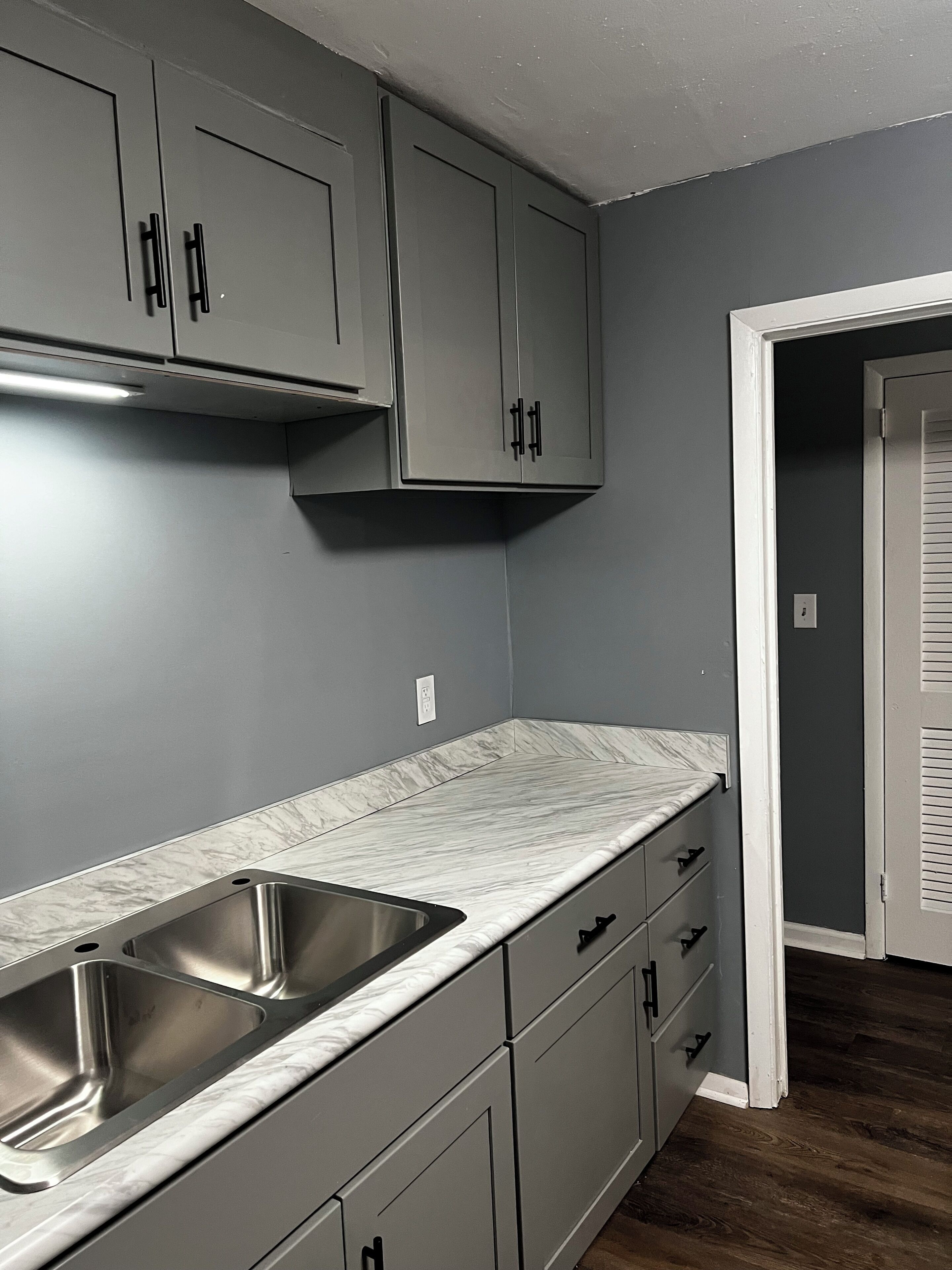 A kitchen with grey cabinets, a stainless steel sink, and a marble countertop.