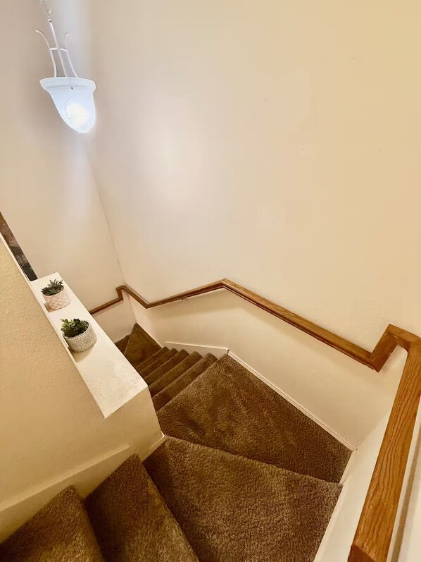 A staircase with a wooden handrail, carpeted steps, and a light fixture above. - Lux Home •Mins To •AT&T Stadium•Six Flags•Texas Rangers•TX Live•Baylor Scott Med (Arlington)