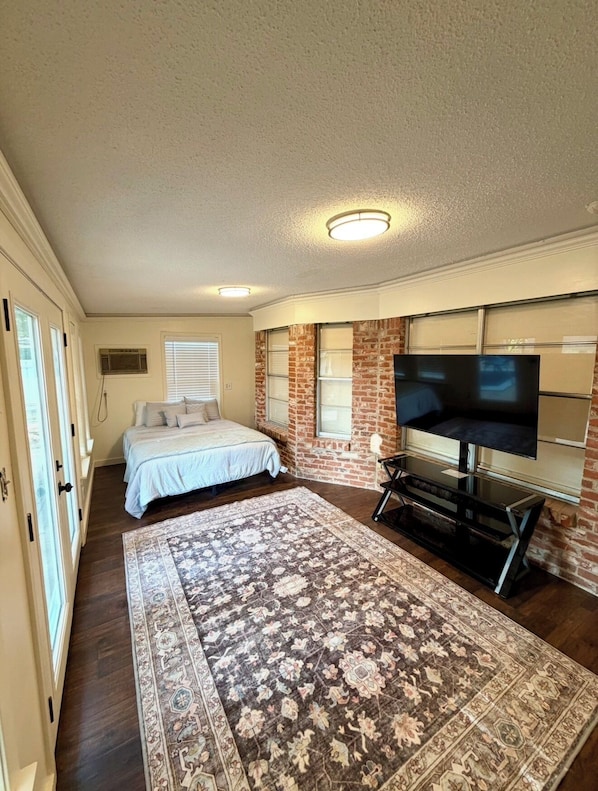 Ein Schlafzimmer mit einem Bett, einem Fernseher, einem Teppich und einer Backsteinwand.