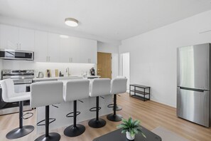 Eine moderne Küche mit weißen Schränken, einem Edelstahl-Kühlschrank und einer Bar mit weißen Hocker.