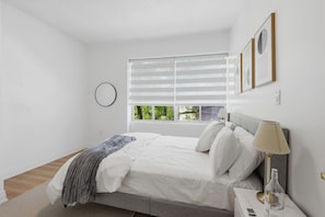 Ein Schlafzimmer mit Bett, Nachttisch, Lampe und Fenster mit Jalousien.