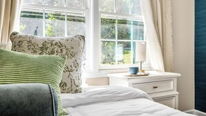 A bedroom with a bed, a nightstand with a lamp, and a window with curtains. - 5Br Lux Green Manor w/Movie Room, Fenced Yard & Sleeps 12 (Raleigh)