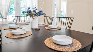 A dining table with white plates, a vase with flowers, and woven placemats. - 5Br Lux Green Manor w/Movie Room, Fenced Yard & Sleeps 12 (Raleigh)
