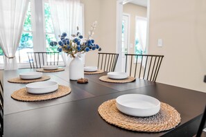 Ein Esstisch mit weißen Tellern, einer Blumenvase und gewebten Platzsets.