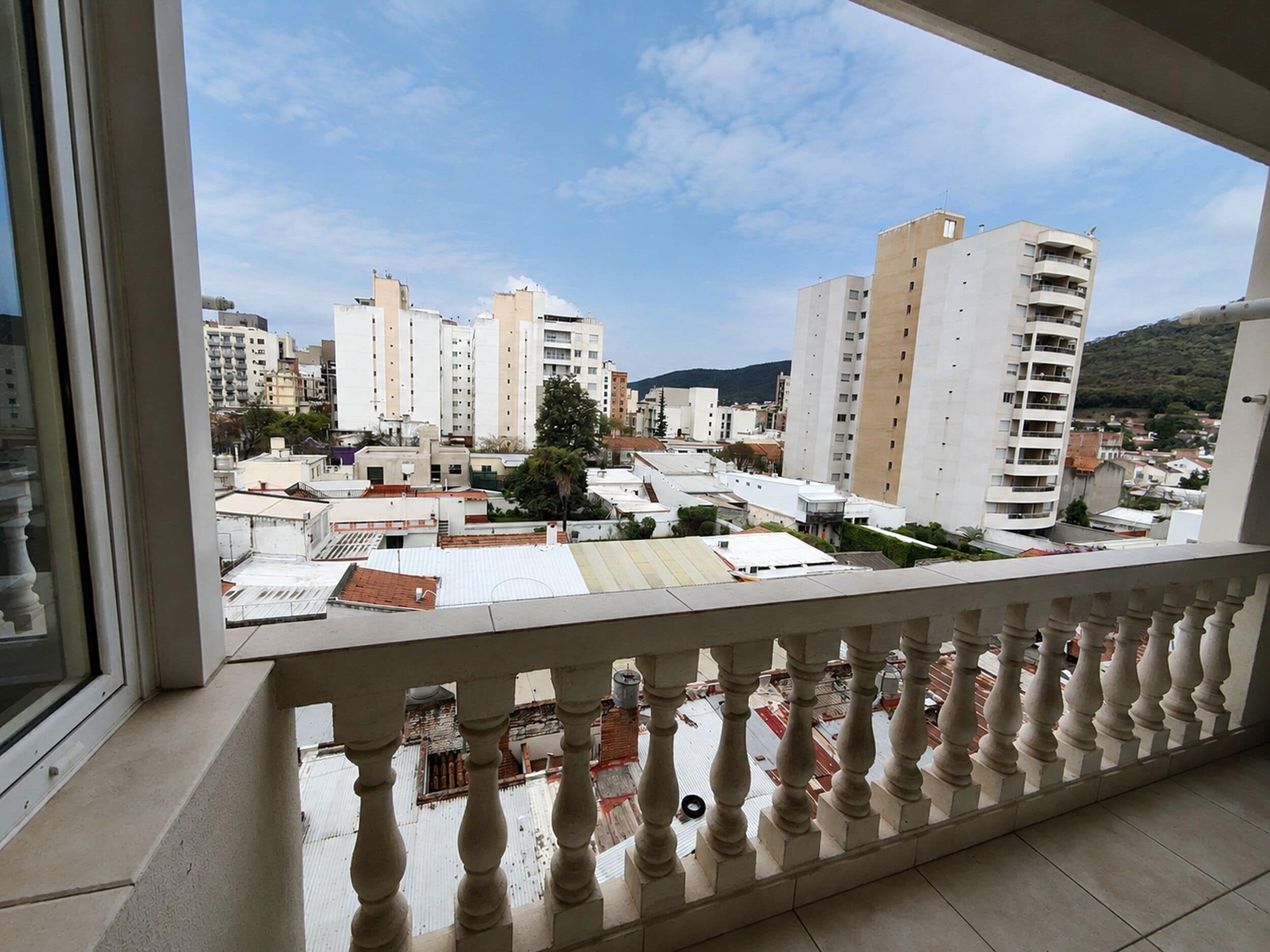 A balcony with a view of a cityscape, including several high-rise buildings and a mountain in the distance.